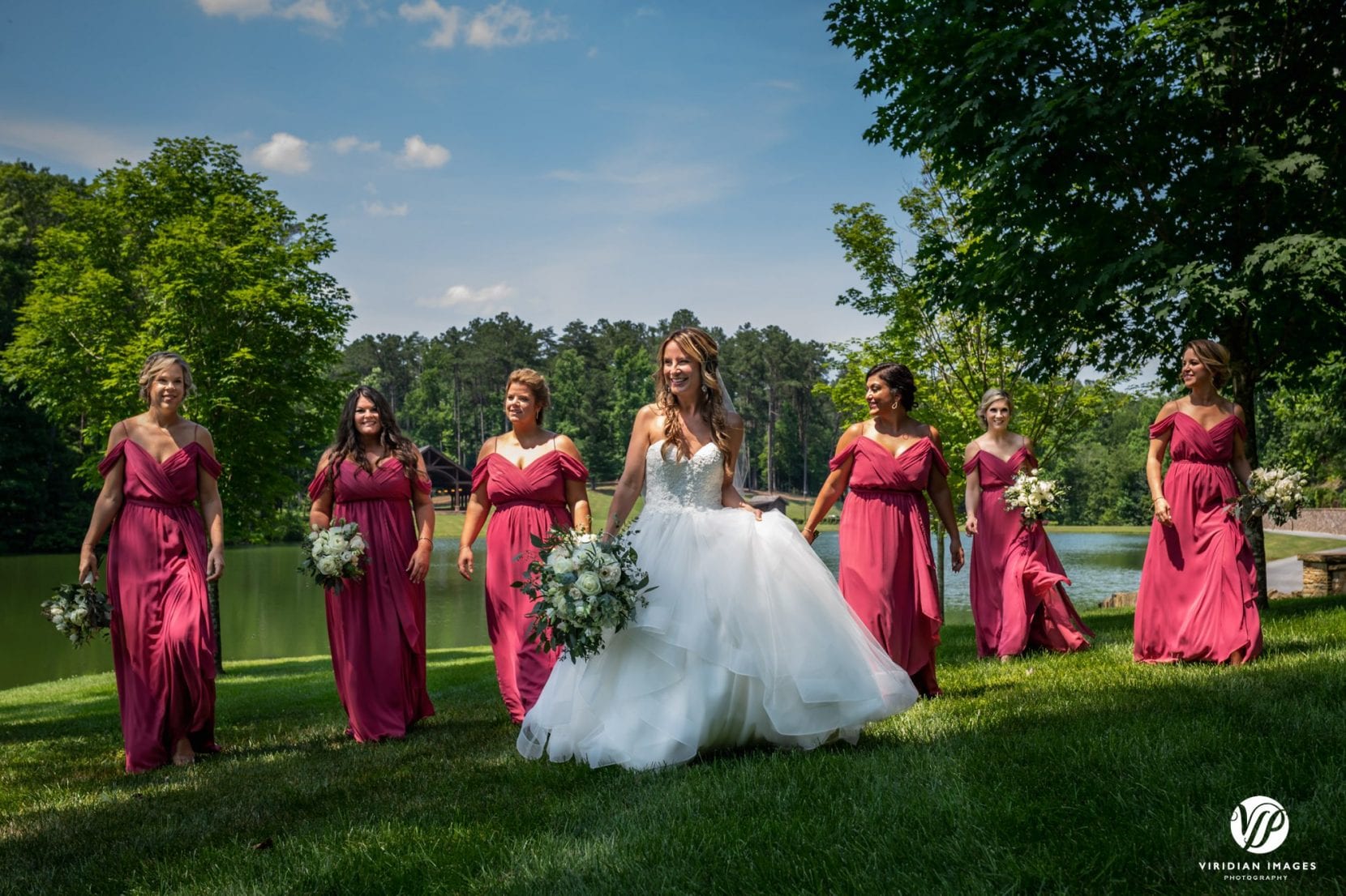 bride and bridesmaids walking on lawn near lake