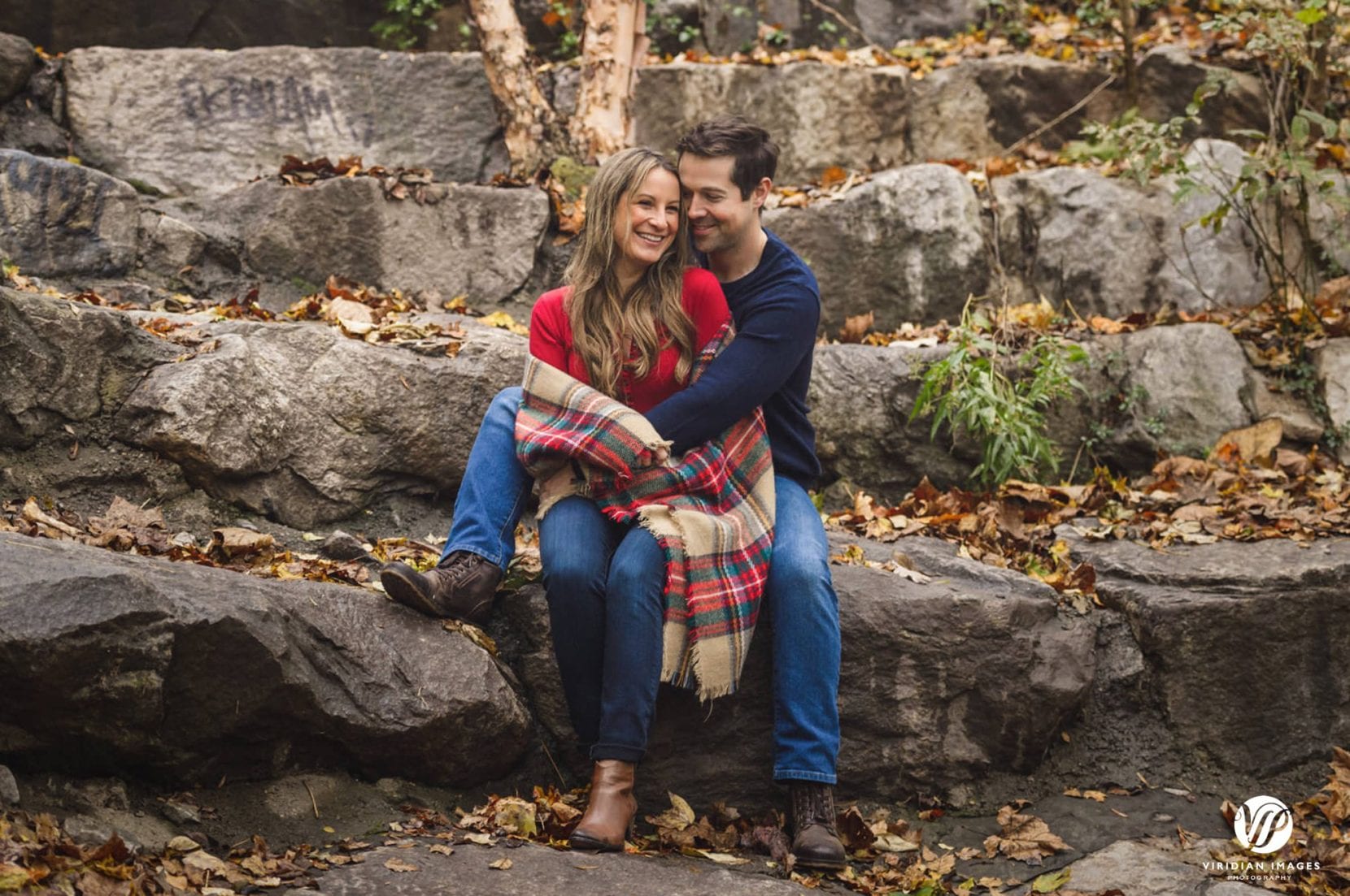 couple sit and embrace on rocks at piedmont park engagement photo