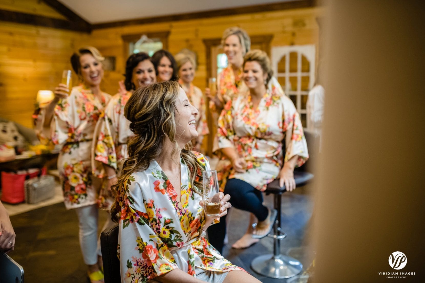 bride drinking champagne with bridesmaids in floral robes laughing