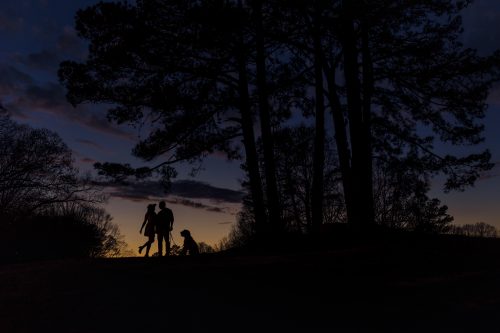 couple and dog silhouette against sunset at lake