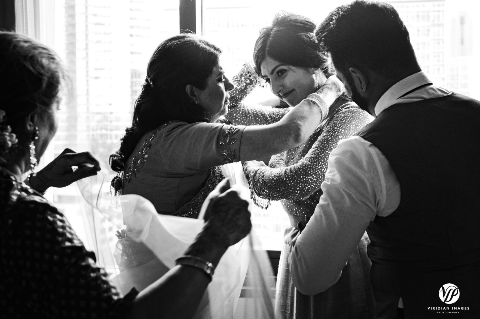 mom putting on bridal necklace on bride