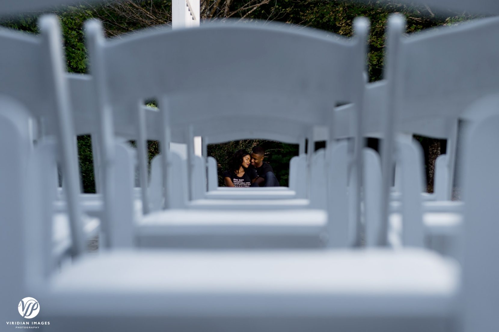 creative shot of couple through white folding chairs prep'd for wedding