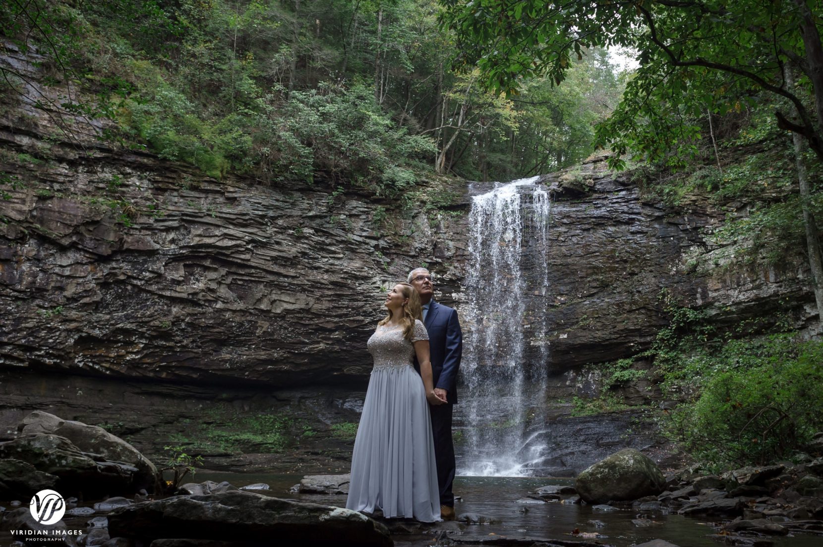  couple looking opposite direction in front of waterfall  during adventure post wedding session at cloudland canyon