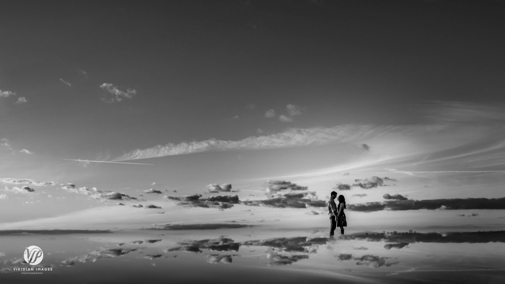 black and white reflection photo of couple facing each other and clouds all around