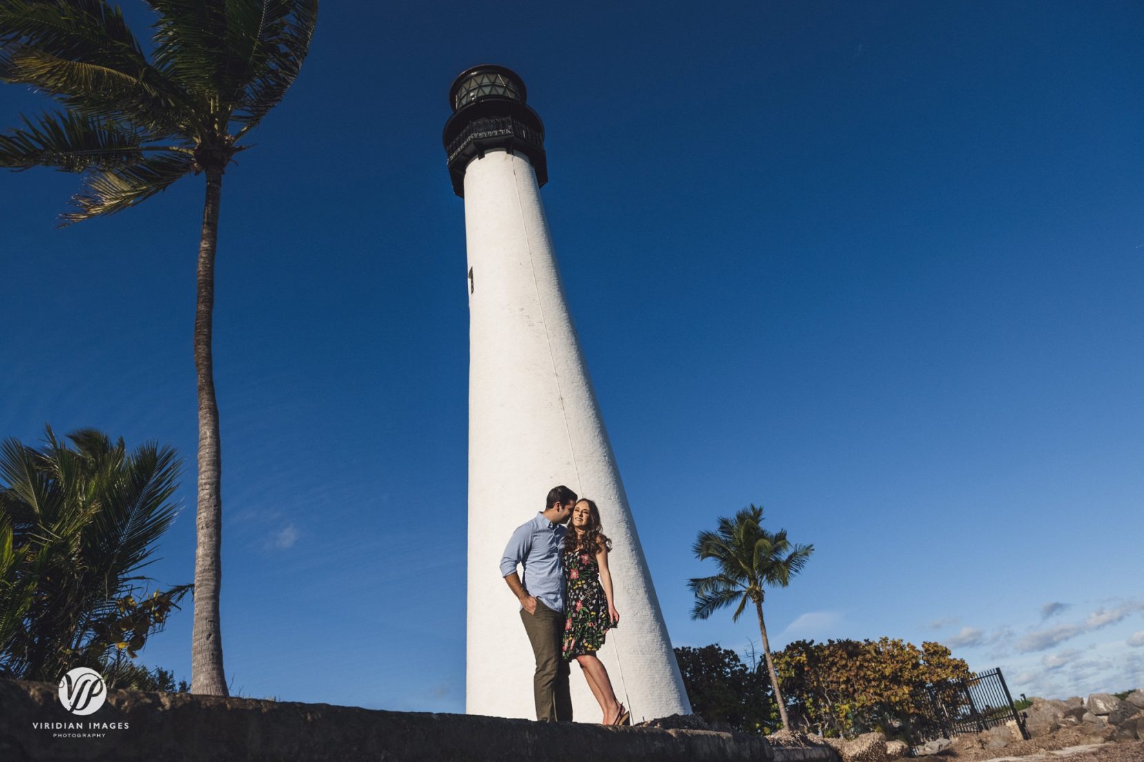 couple hugging against white lighthouse during engagement session