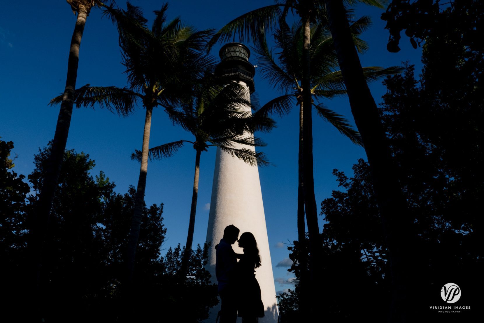 silhouette of couple against white lighthouse with palm trees and blue skies