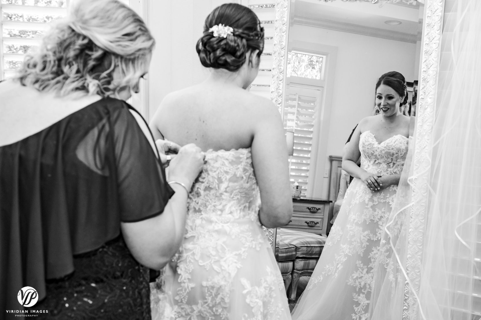 reflection of bride as she's putting on dress with mom's help