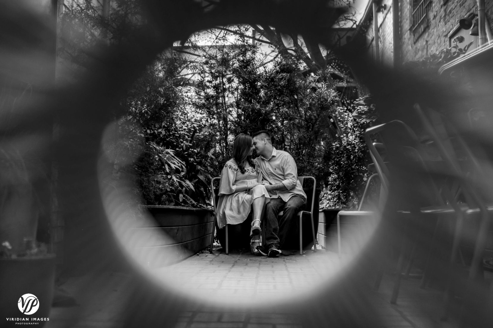black and white photo of couple kissing shot through weaved chair