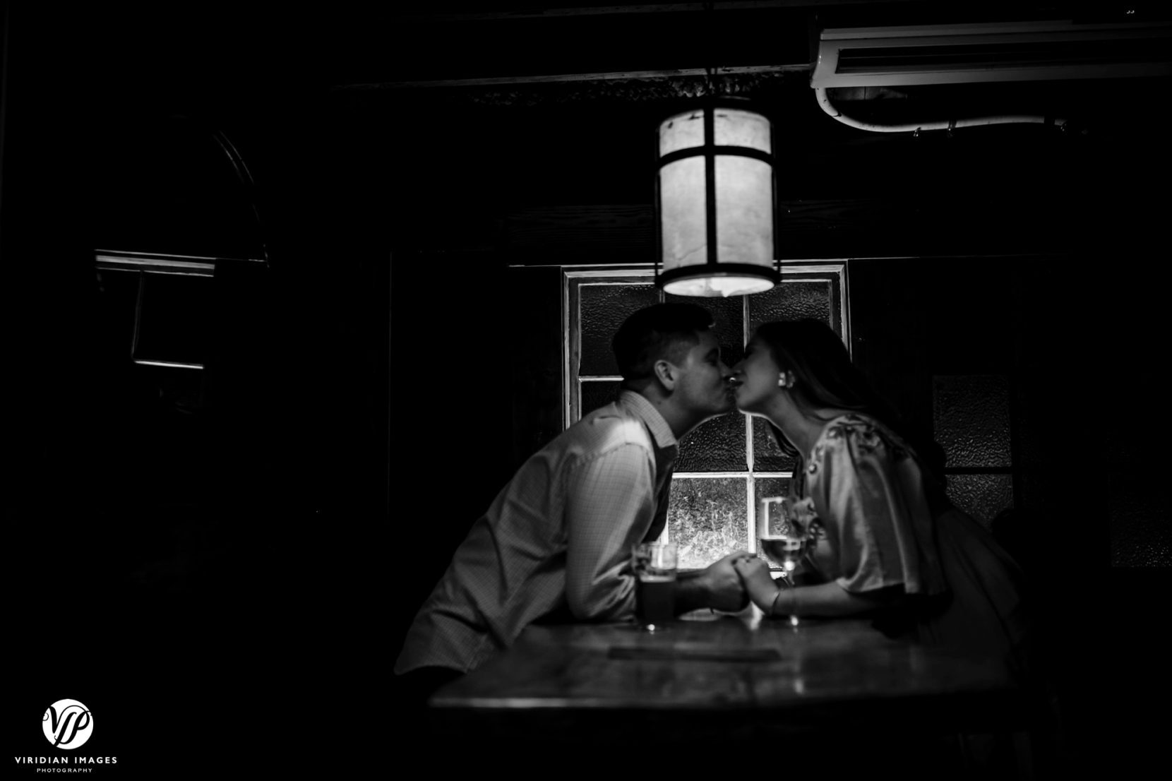 couple kissing across table holding hands at a bar