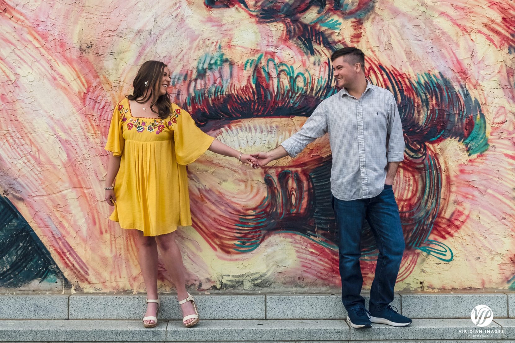 couple holding hands playfully in front of mural