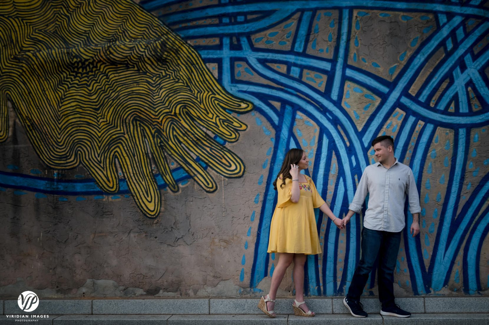 man guiding girl down city street front of mural