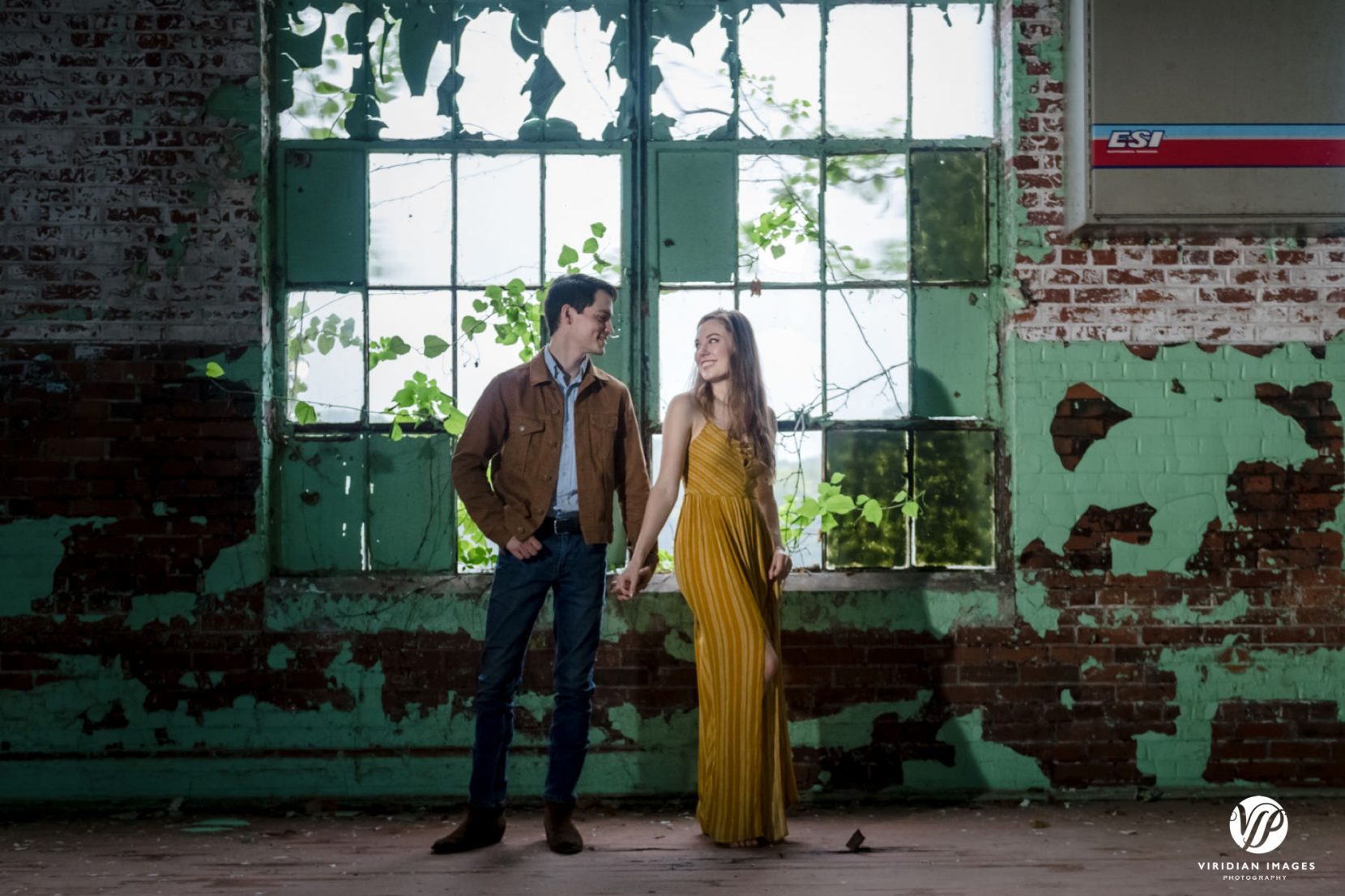 Couple standing and holding hands in front of broken windows and peeled brick wall