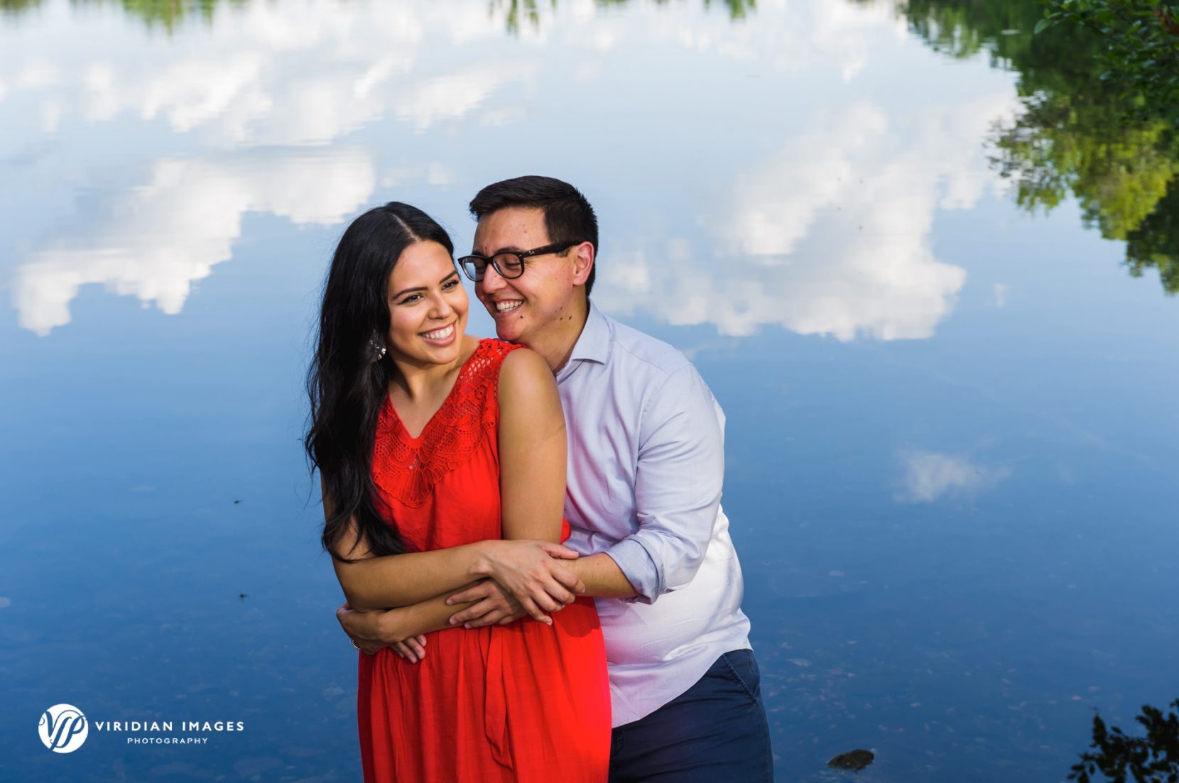 bride to be in red dress with sky and white clouds reflected on lake on top of Arabia Mountain engagement