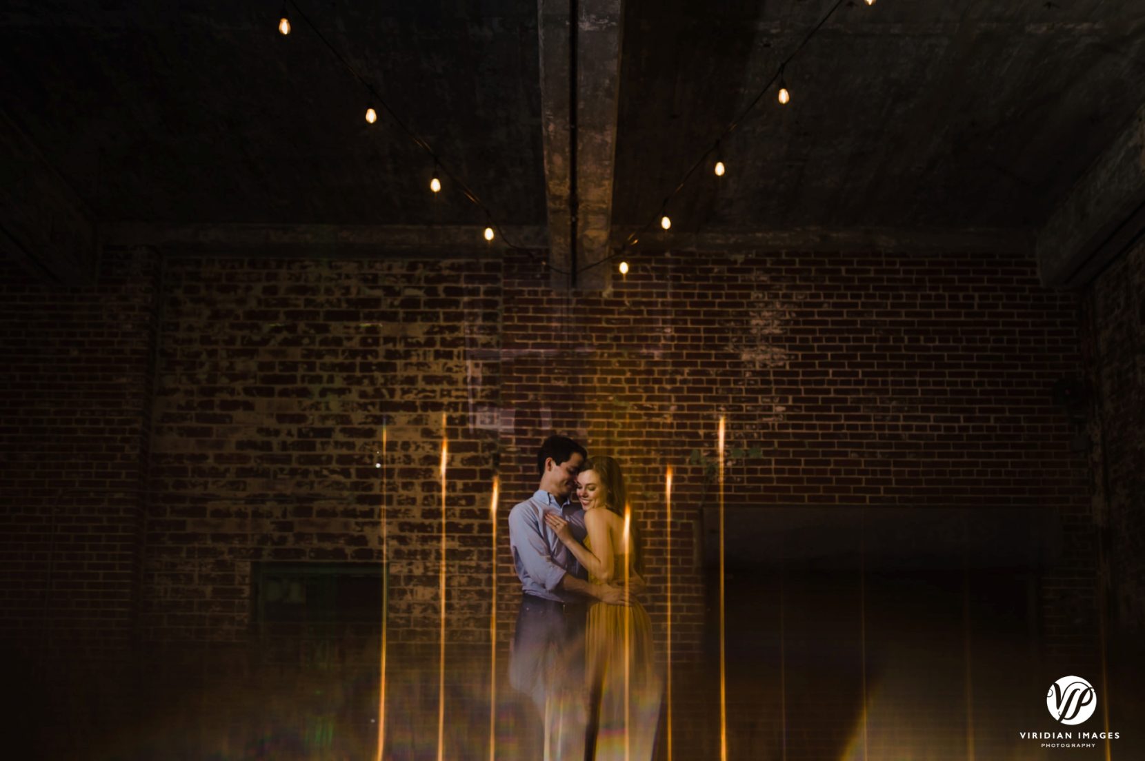 Couple facing each other in a playful way using light streaks with bistro lights
