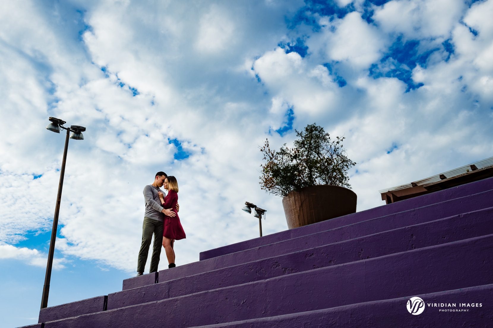 couple standing on purple colored steps with blue skies and puffy clouds in Mason Mill Park Decatur GA
