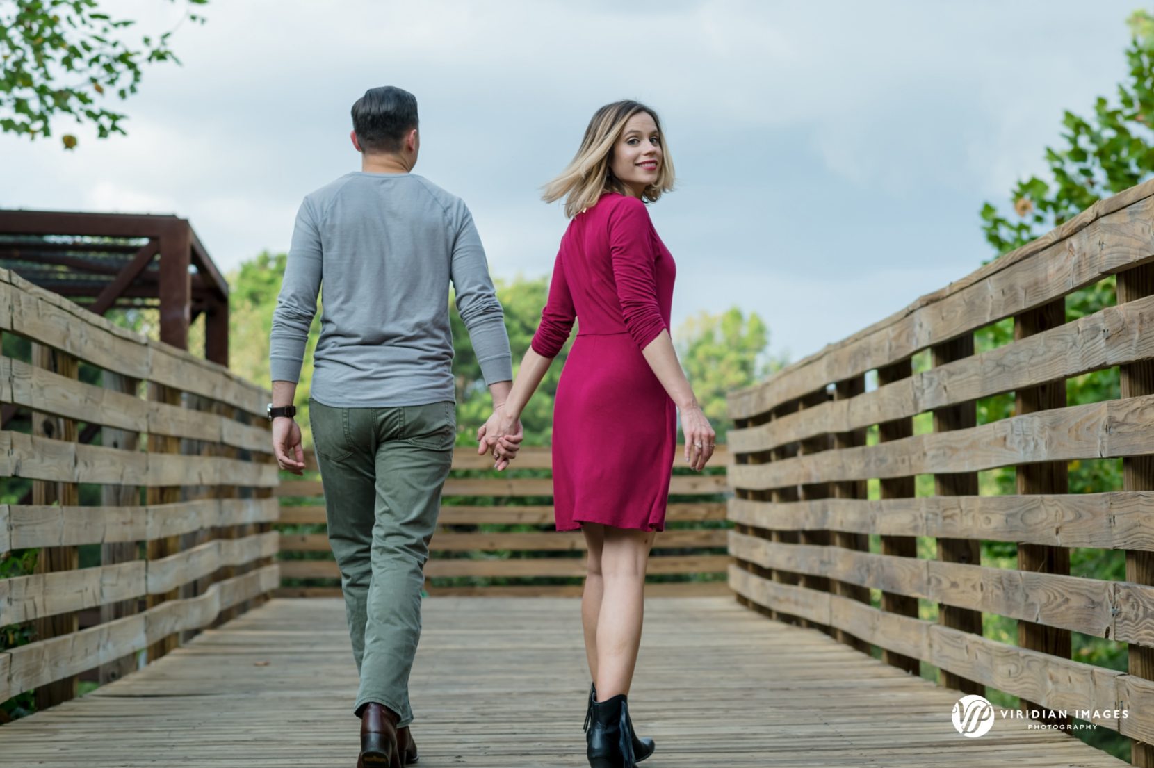 couple walking back and girl looks back on wood boardwalk during engagement session