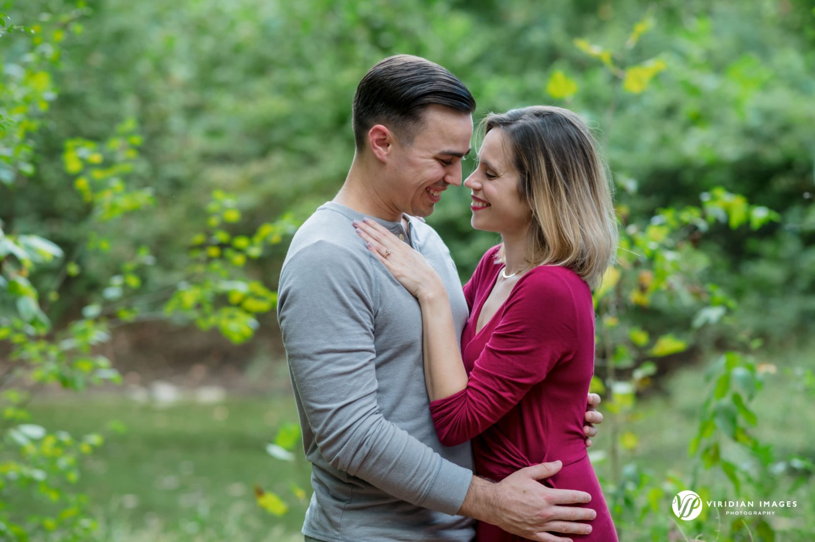 couple hugging and smiling showing engagement ring in front of meadow at Mason Mill Park Decatur, GA 