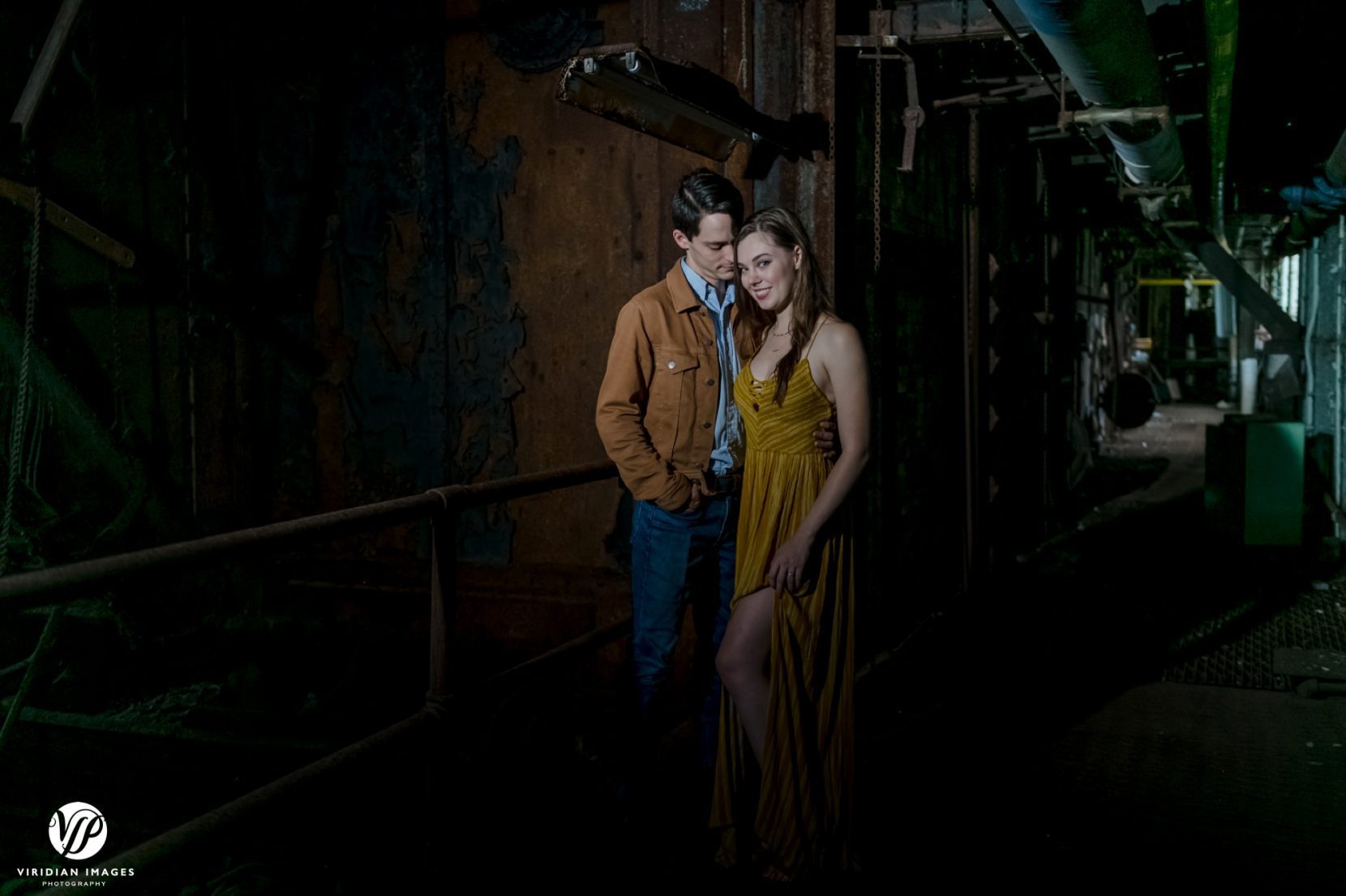 moody portrait of couple on a rusty catwalk inside dark equipment room at Lindale Mill