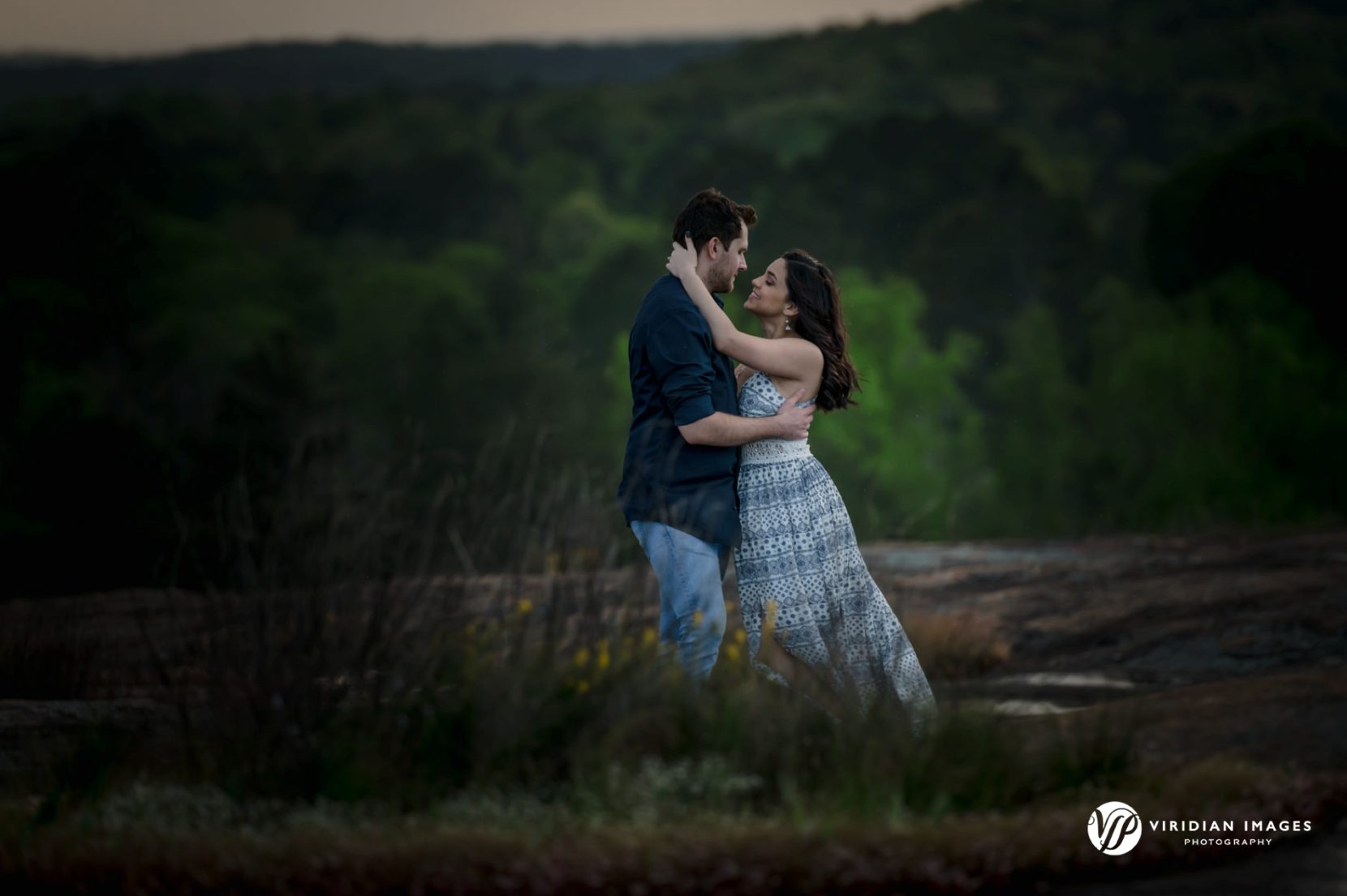 Romantic photo of couple holding each other with trees filling the background in the distance
