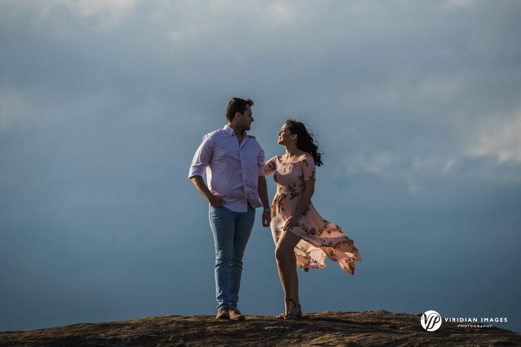 Couple standing on granite Mountain as storm clouds gather in the distance, creating a dramatic scene