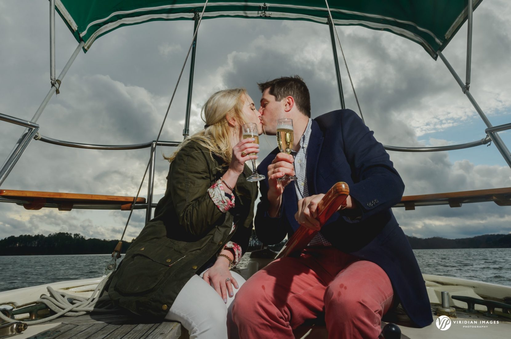 Couple kissing while celebrating on sailboat during engagement session on Lake Lanier