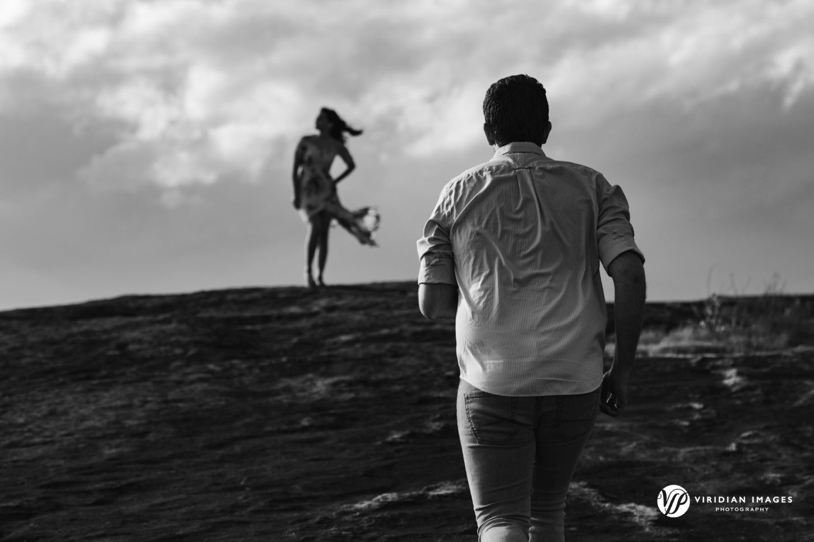 Groom-to-be running towards bride on top of granite Mountain during spring engagement shoot