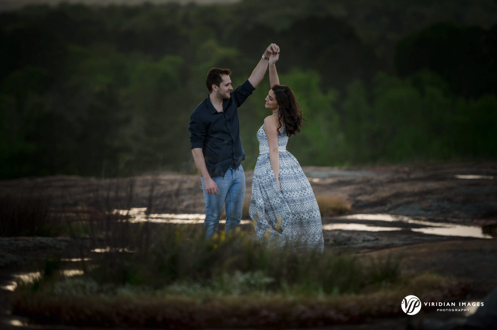 Couple dancing among patches of grass and flora on top of granite terrain during spring engagement photoshoot