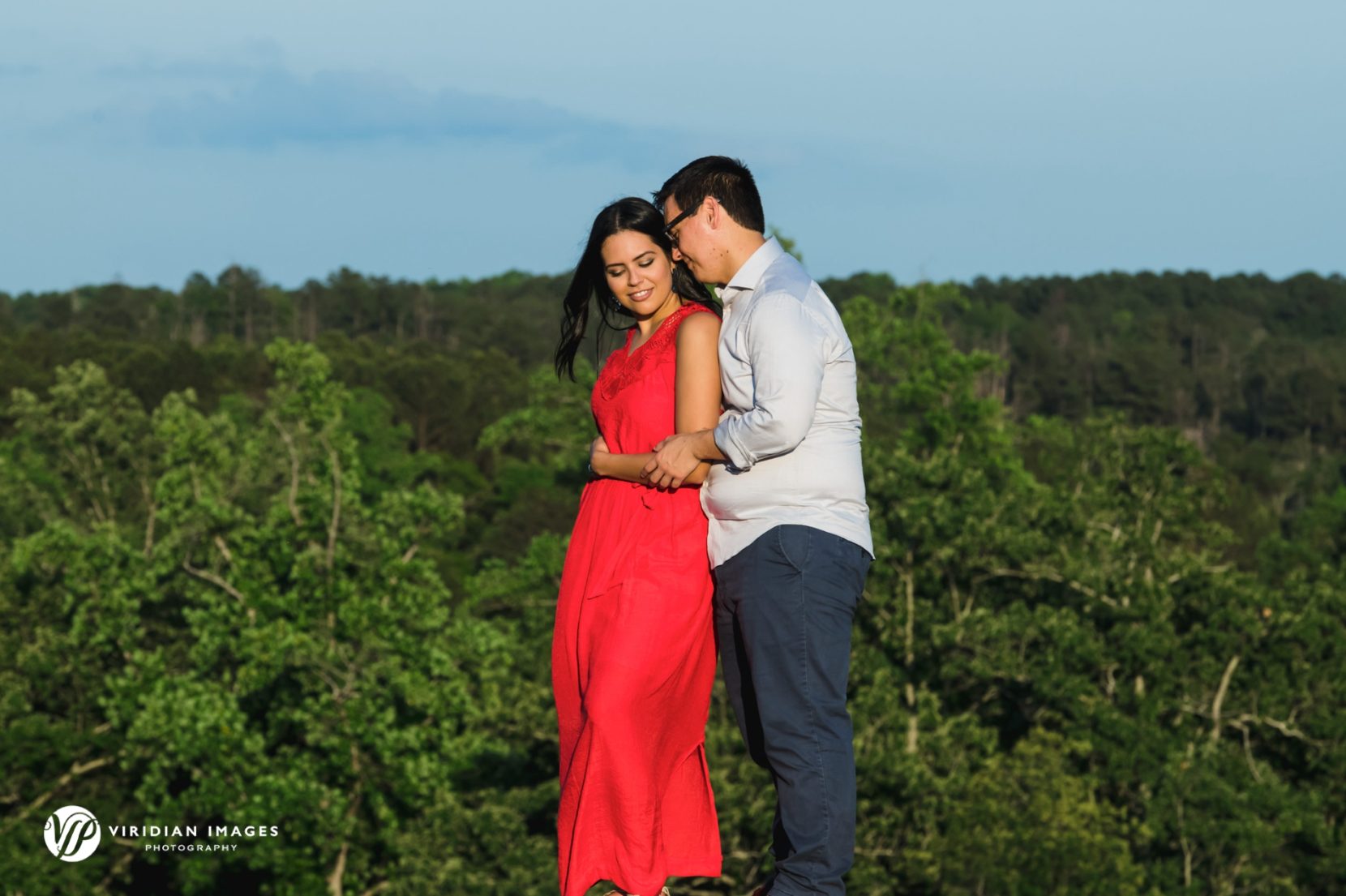 romanic moment of woman in red dress on top of mountain against blue skies and wind blown hair