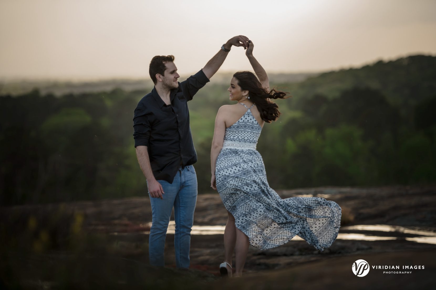 Couple dancing while wind picks up dress at the top of Arabia Mountain during springtime engagement shoot.