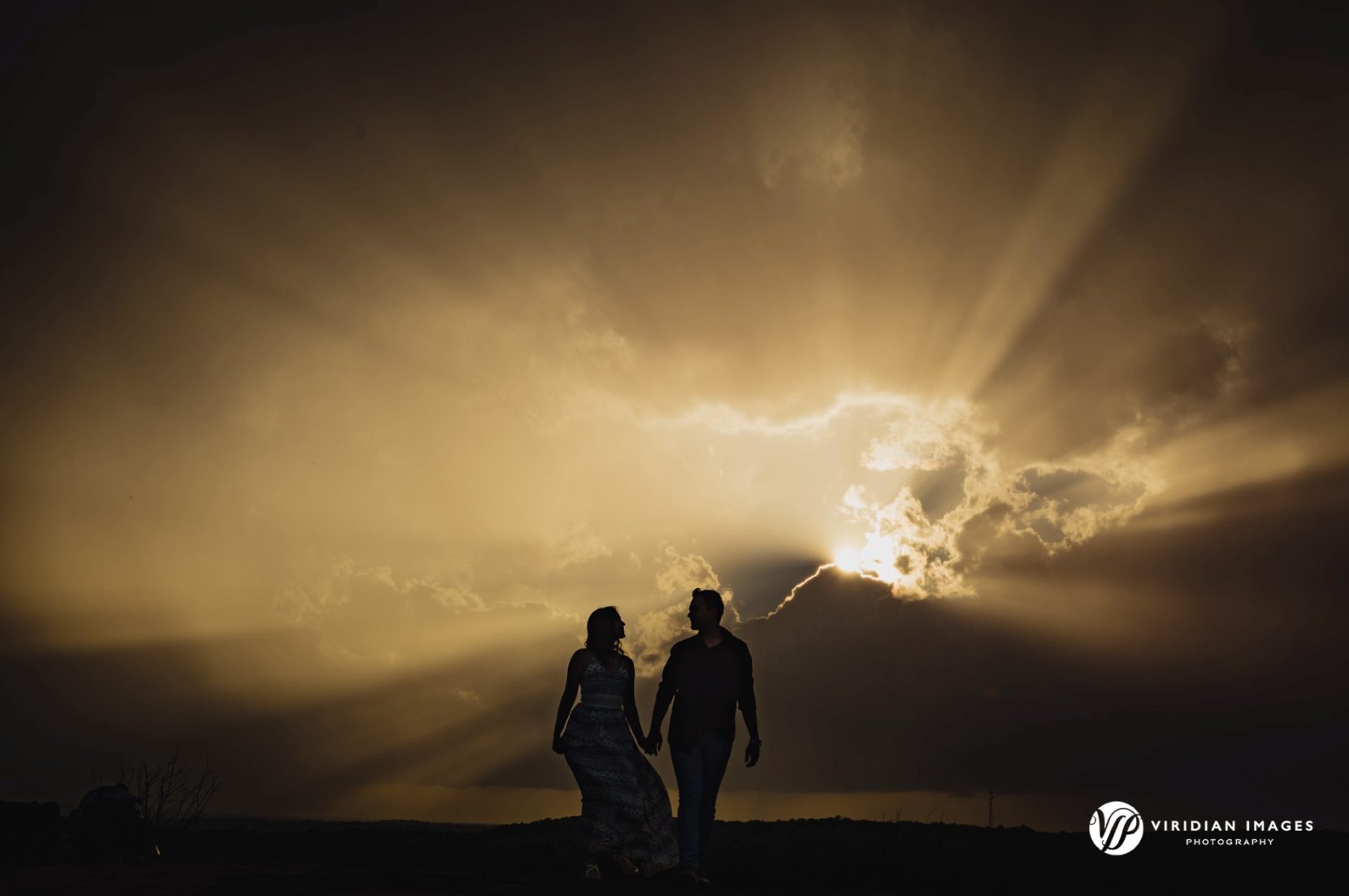Engaged couple silhouetted at the top of Mountain with moody skies during spring engagement session