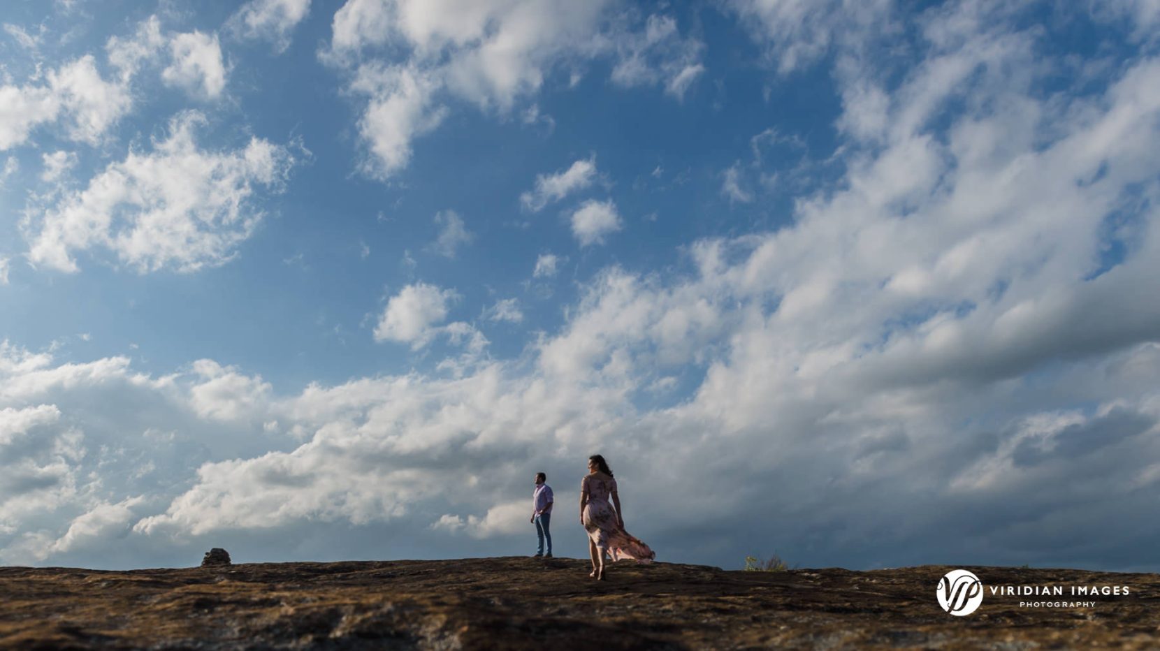 Wide shot of small couple against big sky on top of granite Mountain during spring engagement session