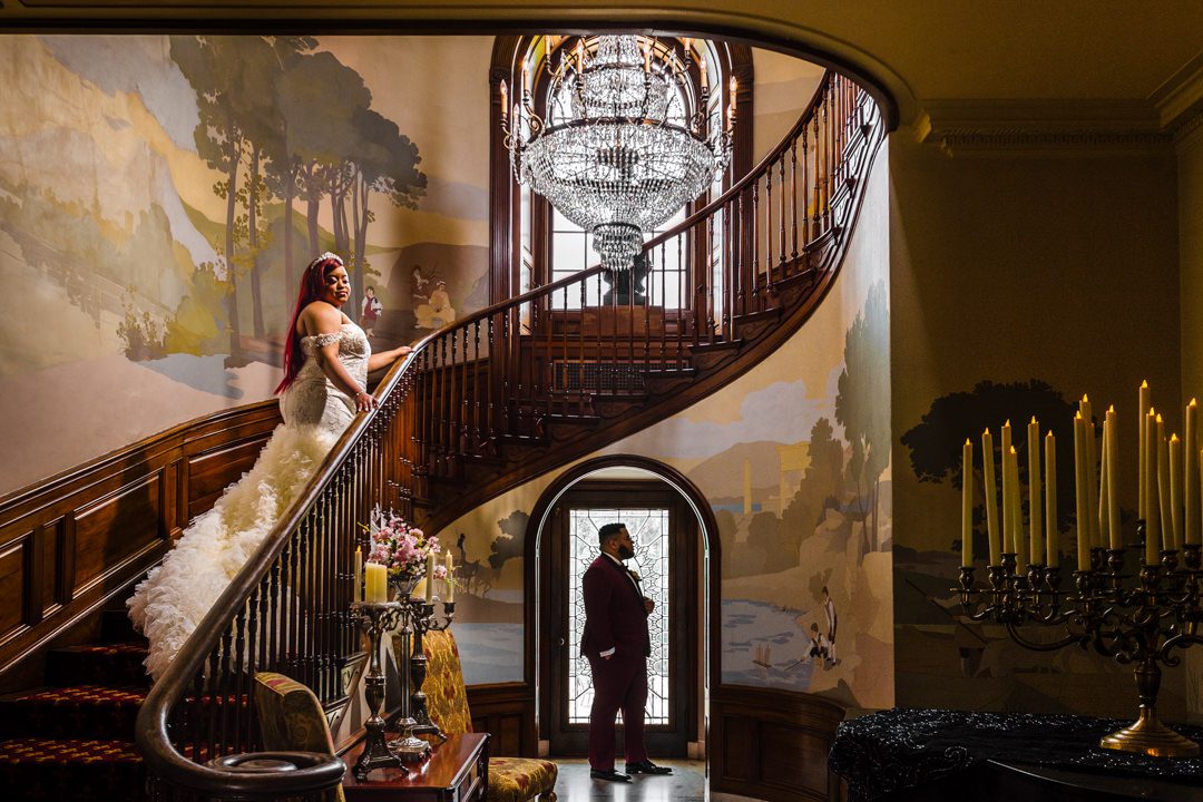 artistic wedding couple portrait on grand muraled staircase at the tate house. groom below silhouetted by glass door