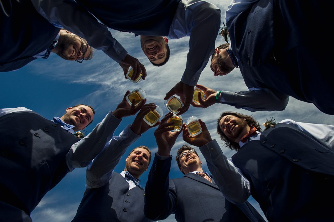 groomsmen drinking shot from below with blue skies above