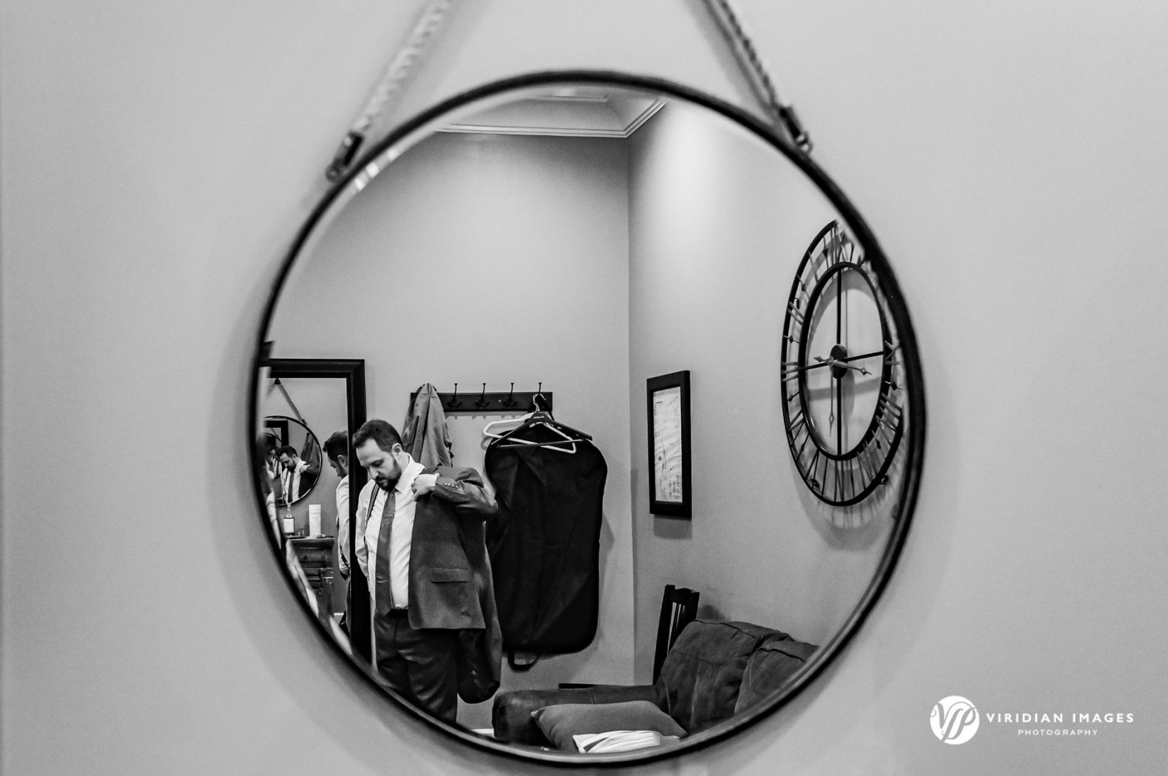 Reflection of groom putting on suit jacket while getting ready for his wedding