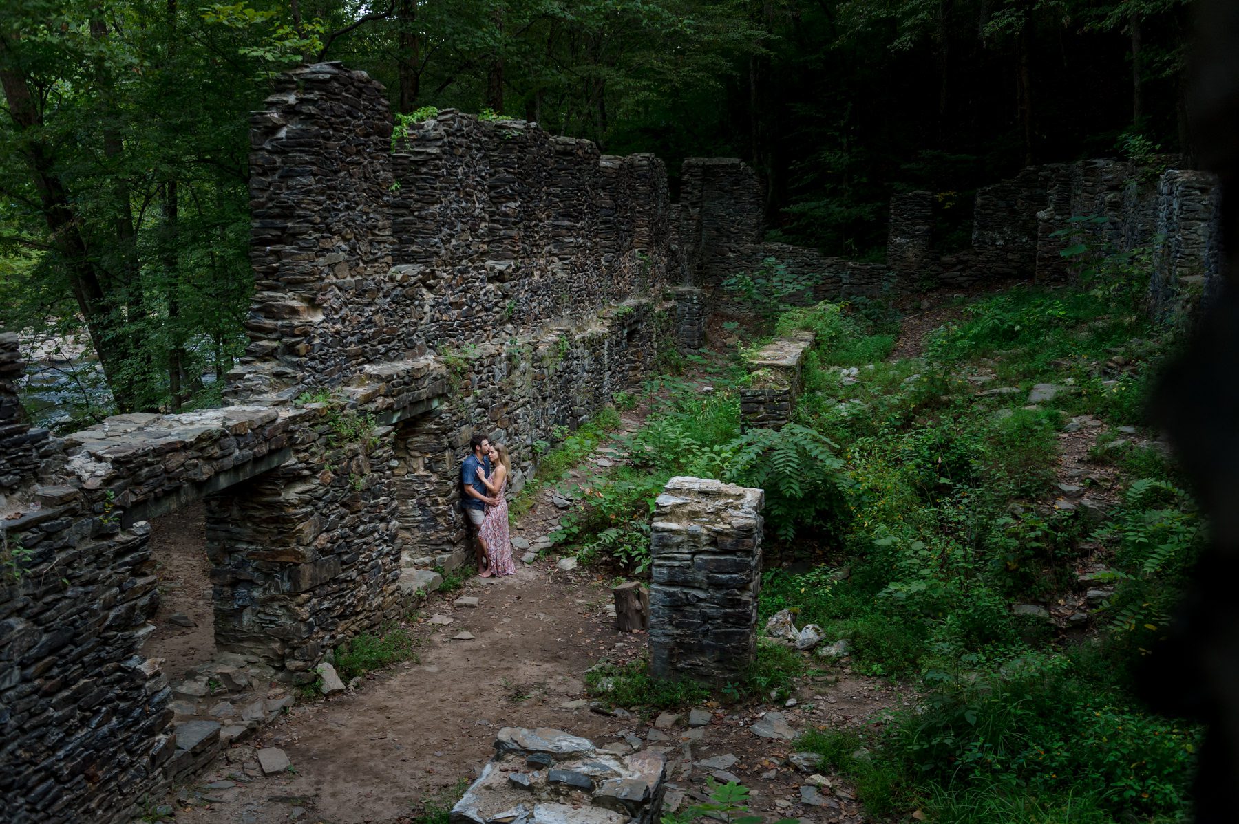 Pulled out wide photo of couple against weathered stone wall at Sope Creek