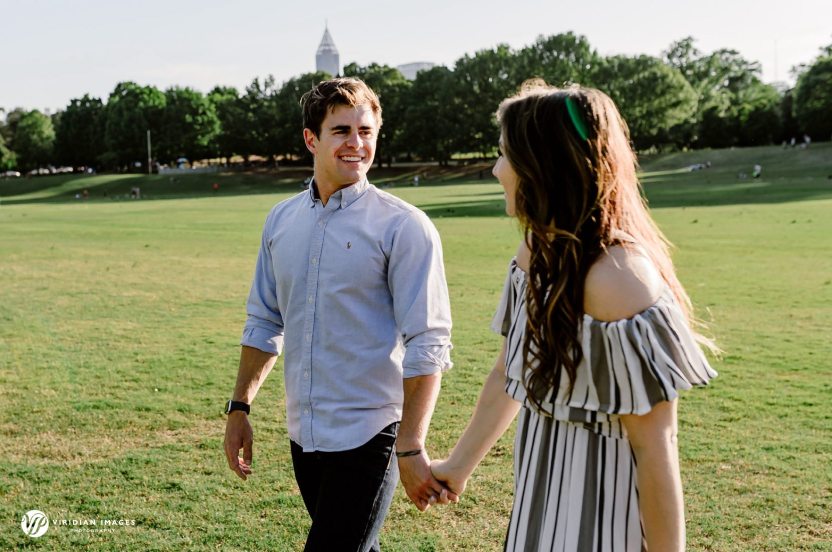Couple walking hand in hand on Piedmont Park meadow during late afternoon engagement session