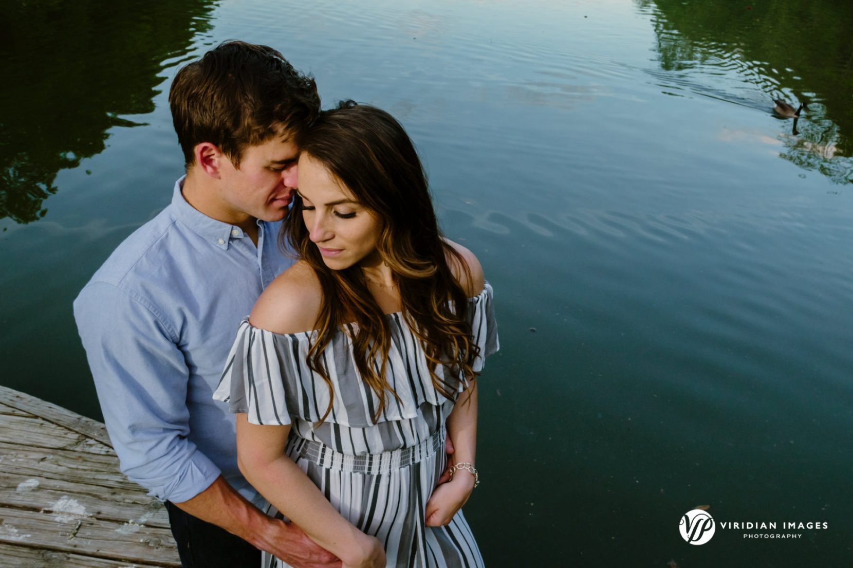 Couple lit with off-camera flash with sky reflection on lake during blue hour at Piedmont Park Atlanta engagement session