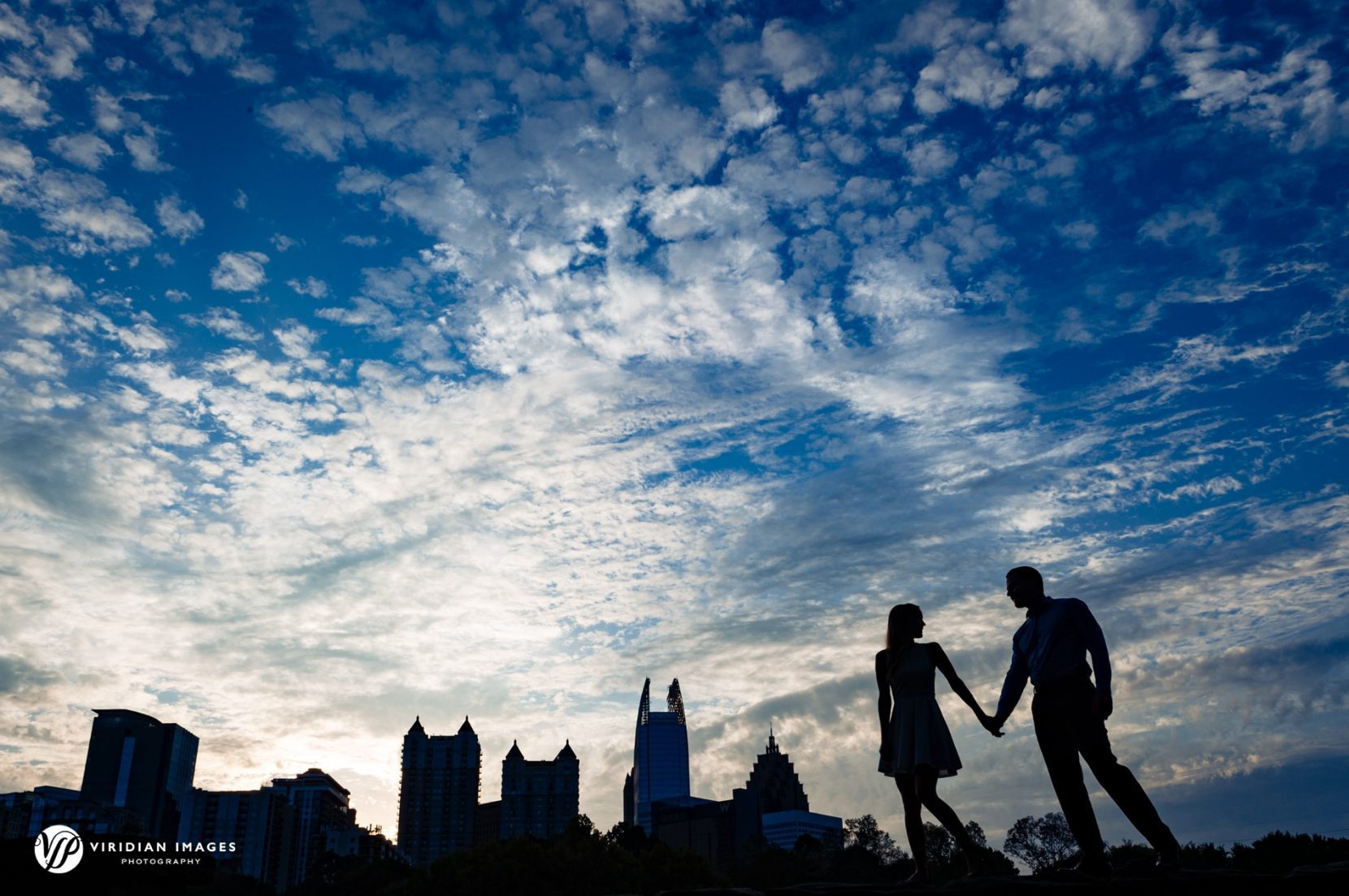 Abbey and Justin sharing a walk with Atlanta skyline background during their Piedmont Park engagement session