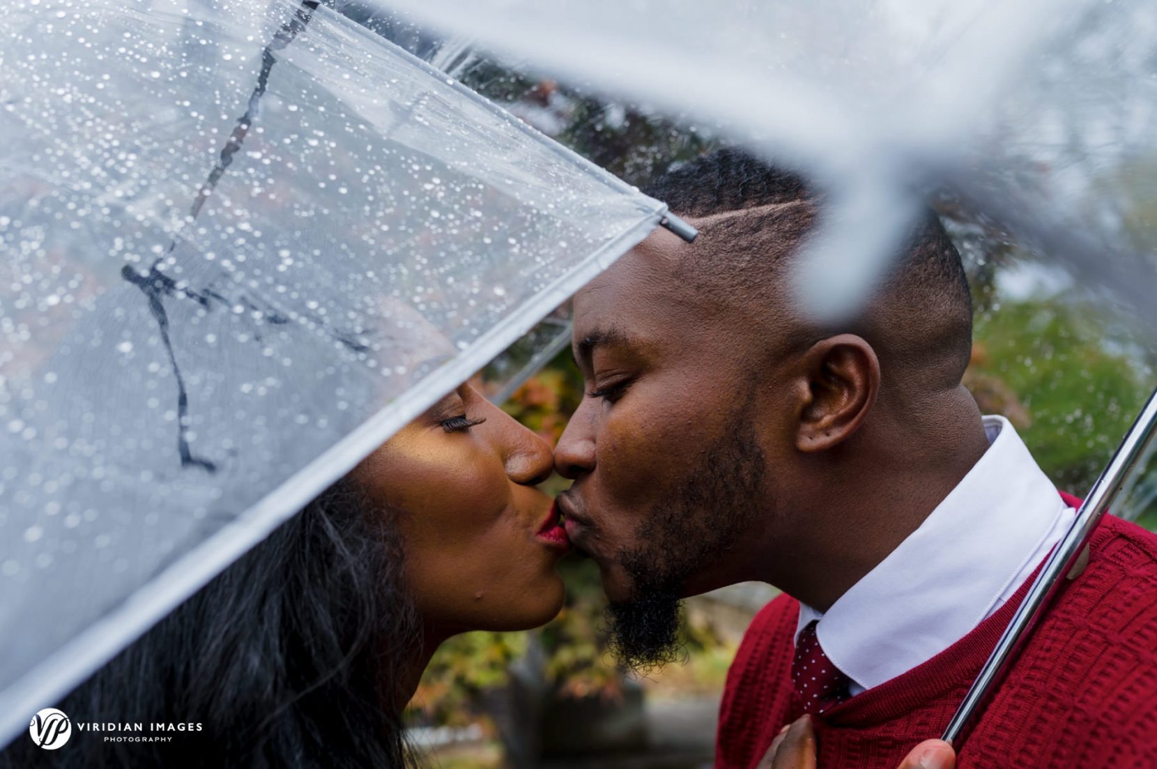 Couple kissing under clear umbrella during rainy-day Oakland Cemetery engagement session in Atlanta