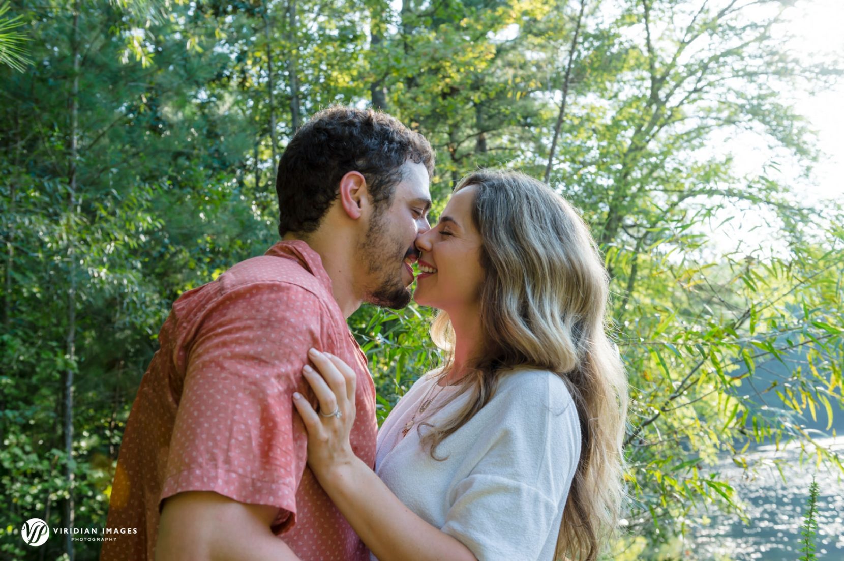 Couple stealing a kiss during engagement session on wood deck along lake at Sope Creek