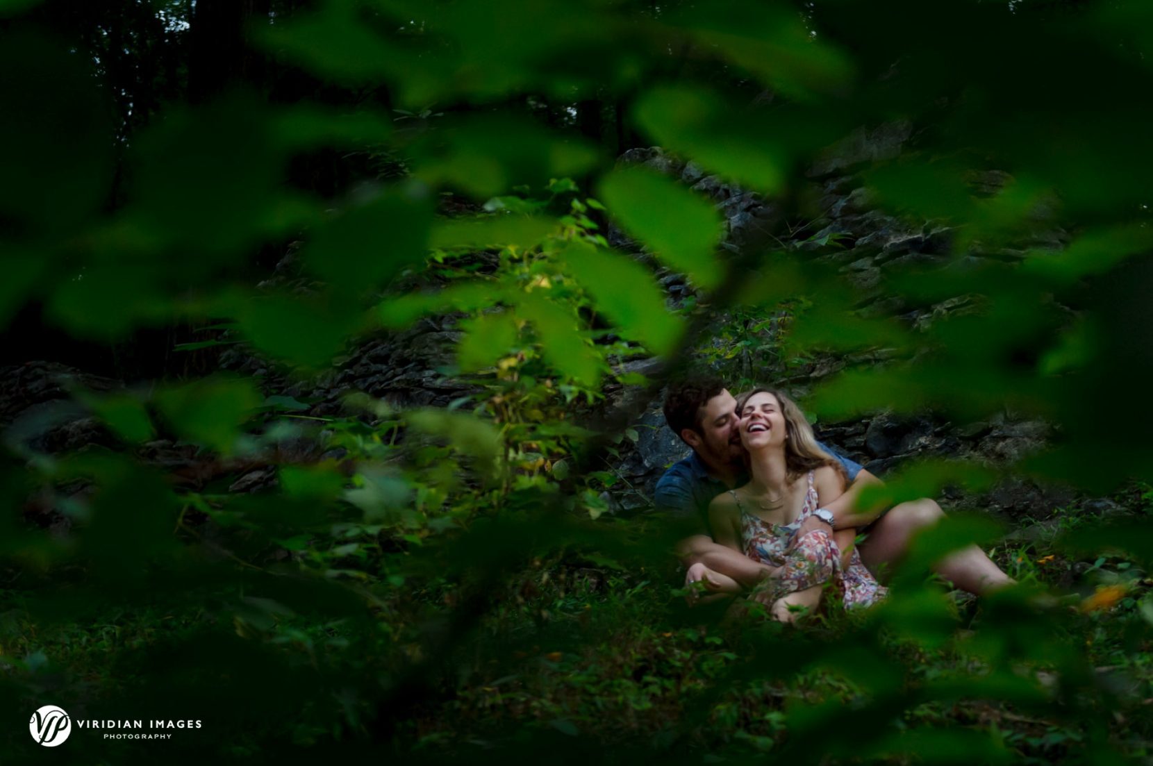 Engaged couple laughing and shring a candid moment among the green foliage during engagement session at Sope Creek