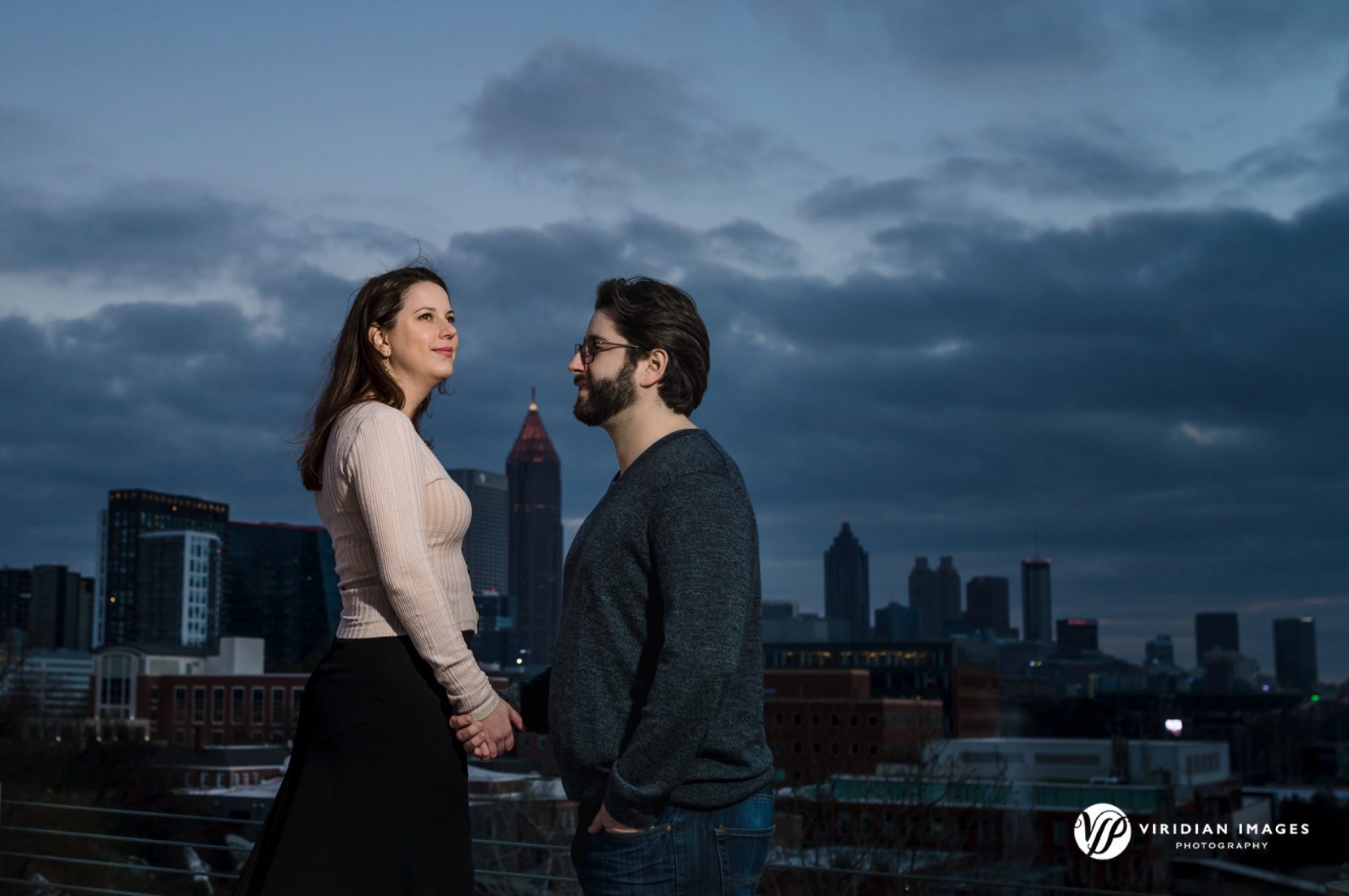 engaged couple holding hands in front of Atlanta city skyline at dusk
