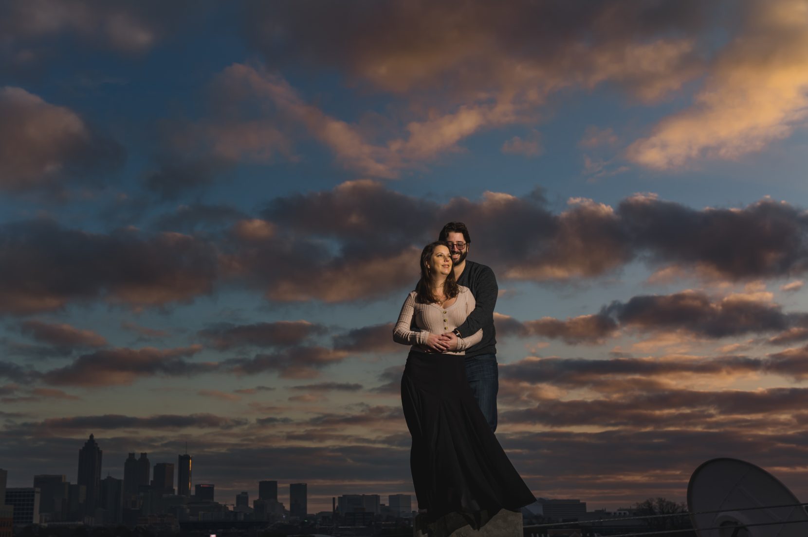 Couple portrait at sunset against beautiful skies and city skyline at the bottom