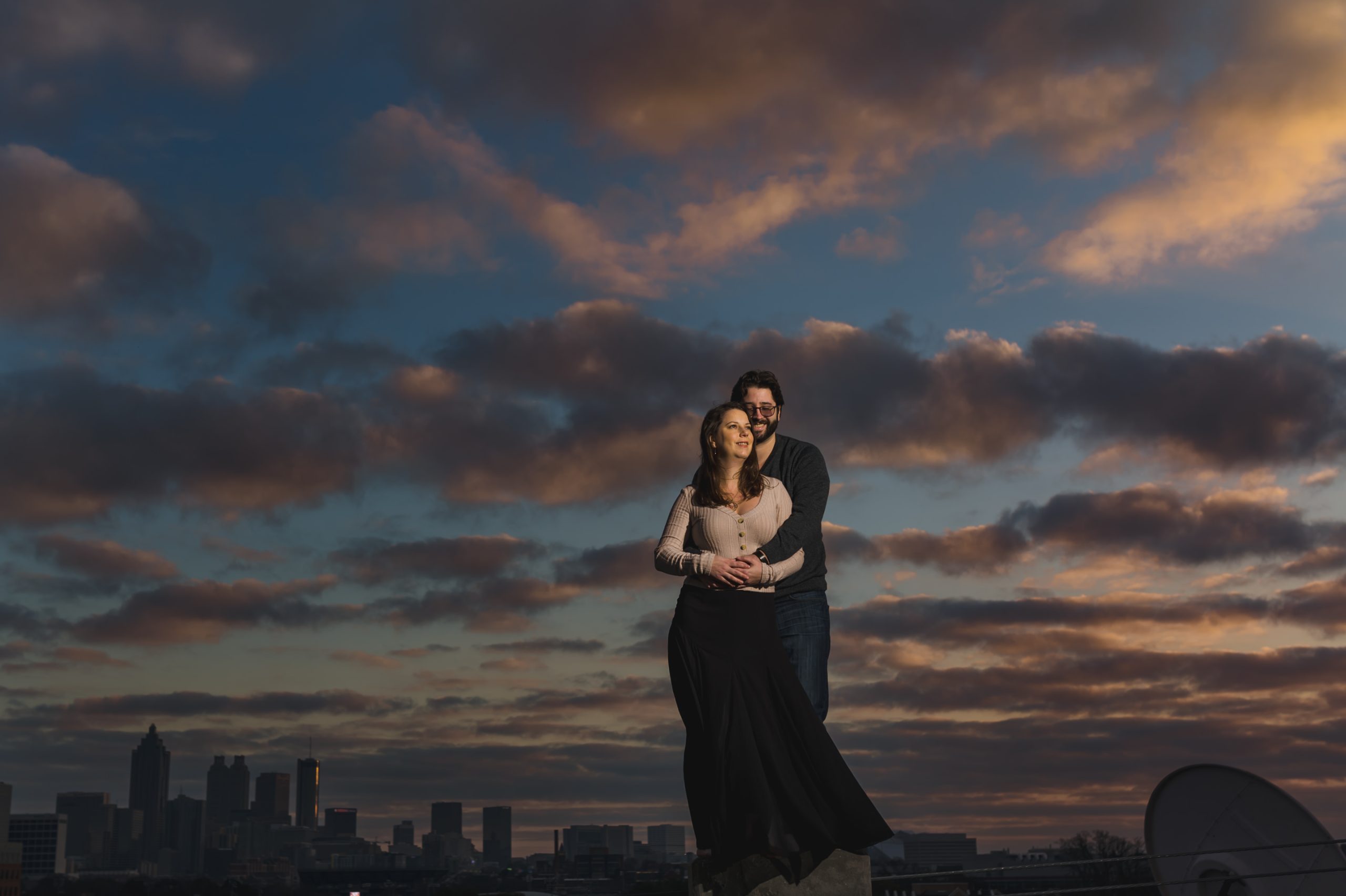 Couple portrait at sunset against beautiful skies and city skyline at the bottom