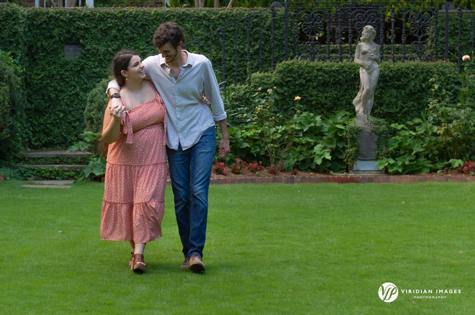Engaged couple walking through grassy open space in Founders Garden at UGA North Campus in Athens, GA.