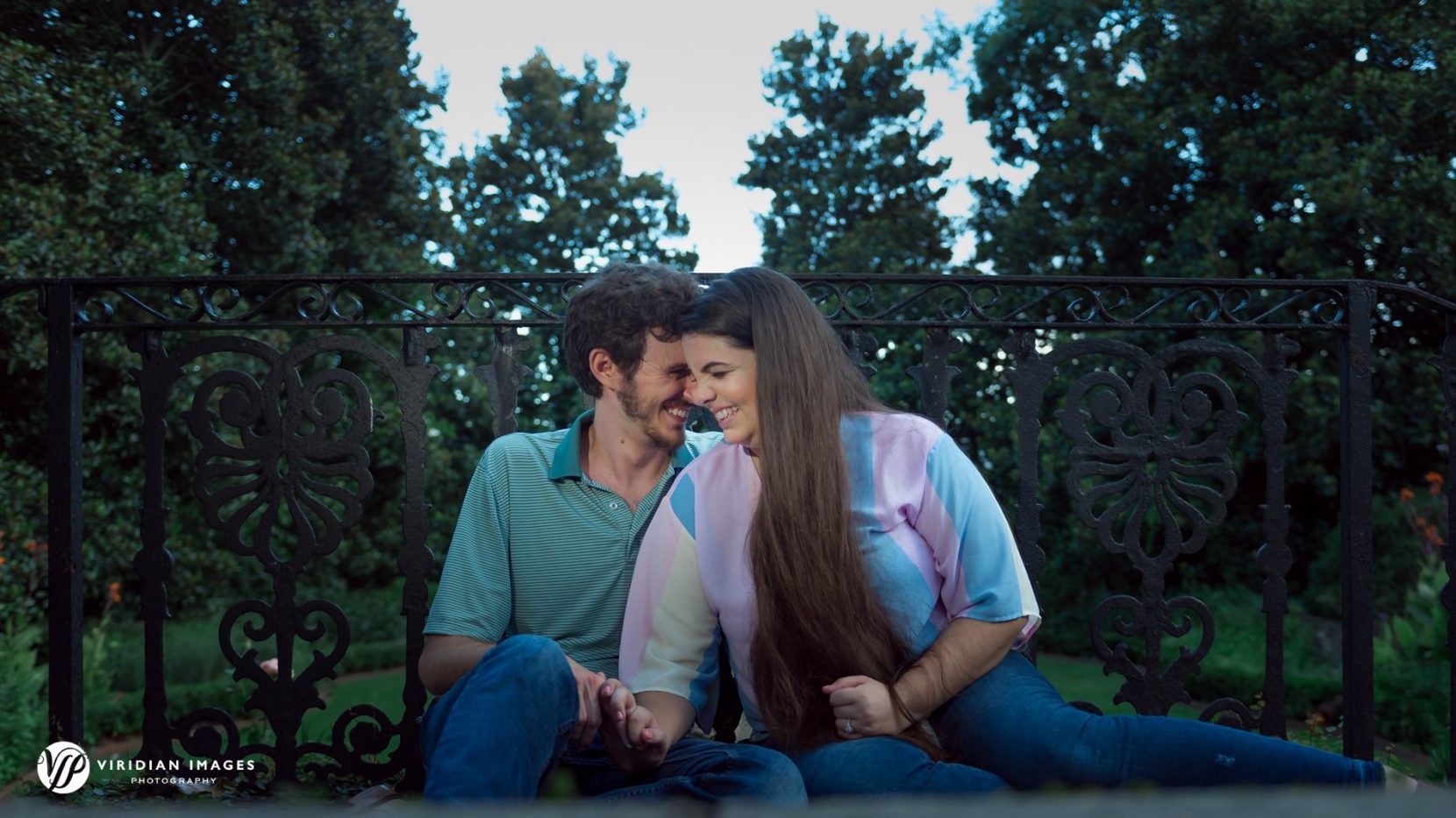 Engaged sitting against iron fence during engagement session at UGA north campus