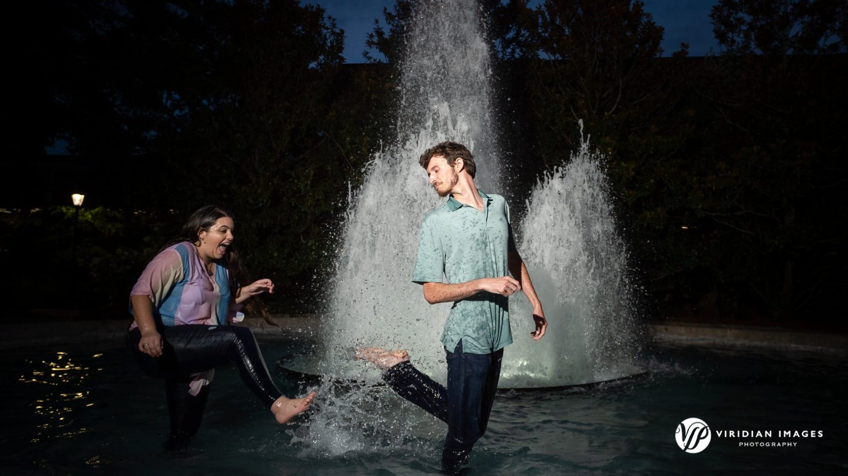 Engaged couple splashing inside fountain at UGA north campus at night