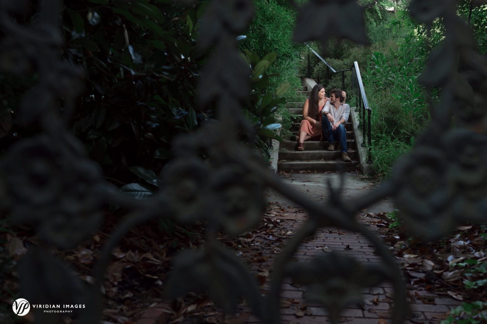 Couple talking under shaded trees with lush summer foliage at Founders Garden during engagement session.