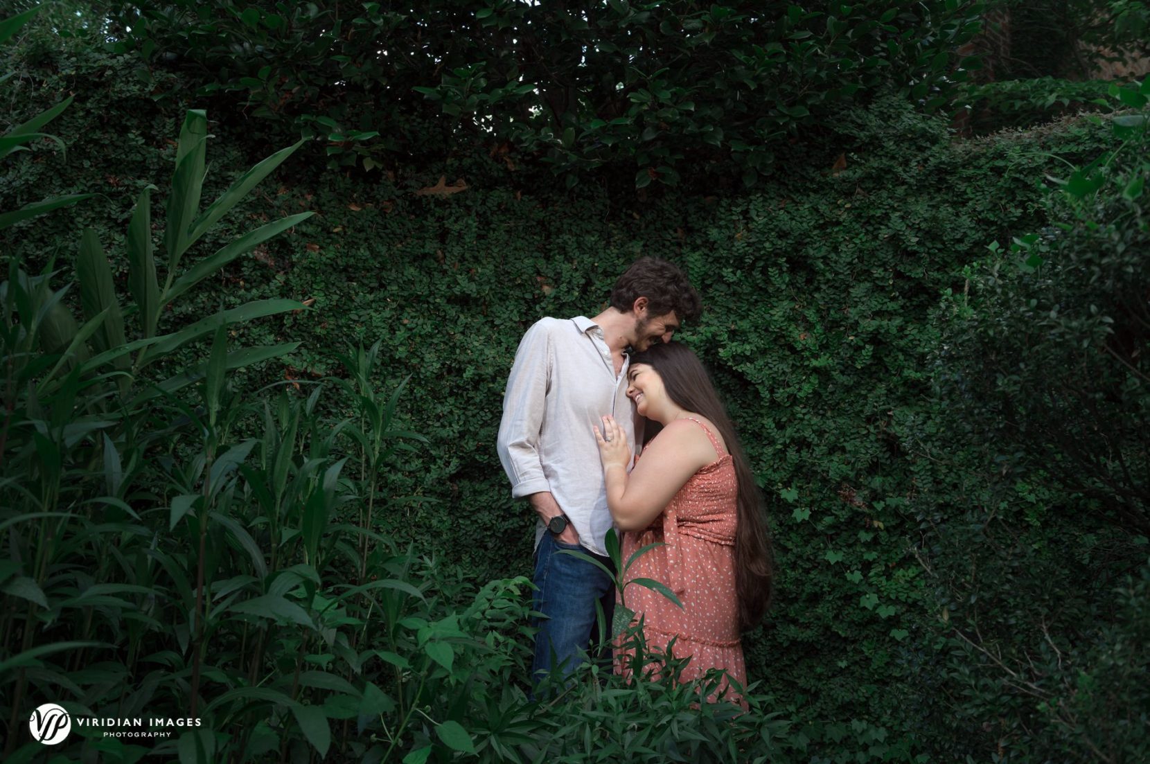 Couple embrace against green foliage wall at UGA north campus engagement
