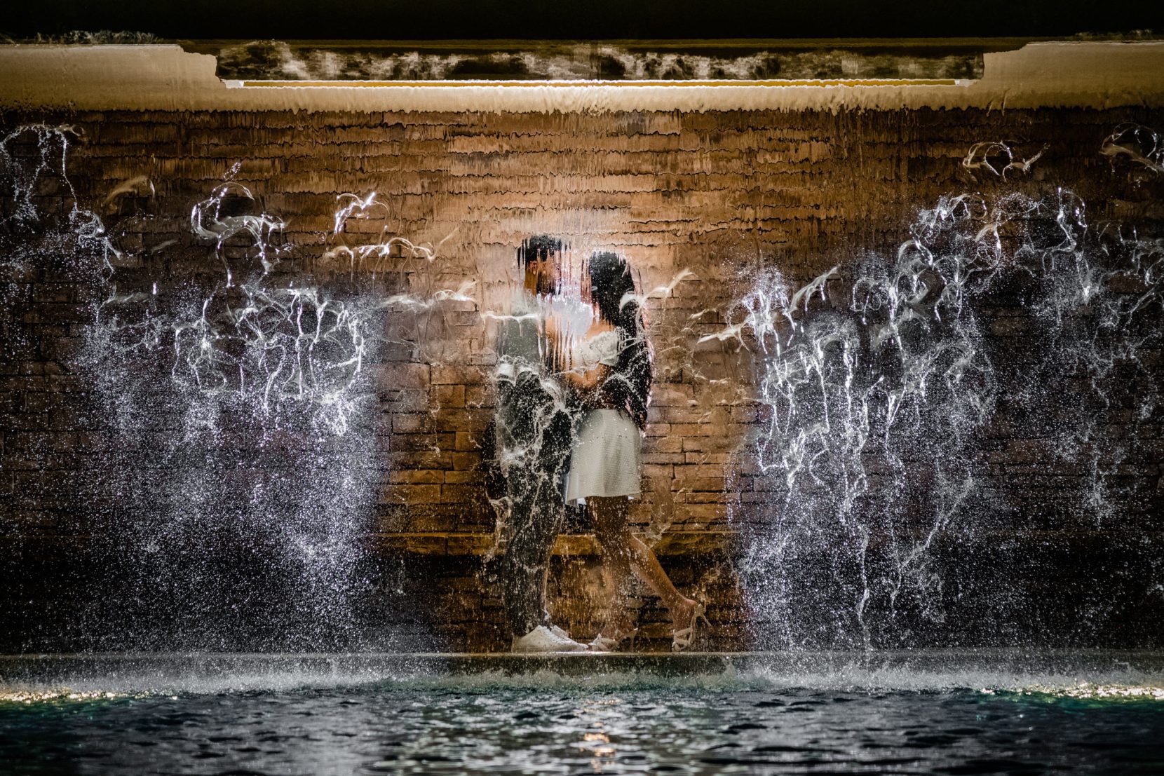 Engaged couple romantic behind pool waterfall in midtown Atlanta at night